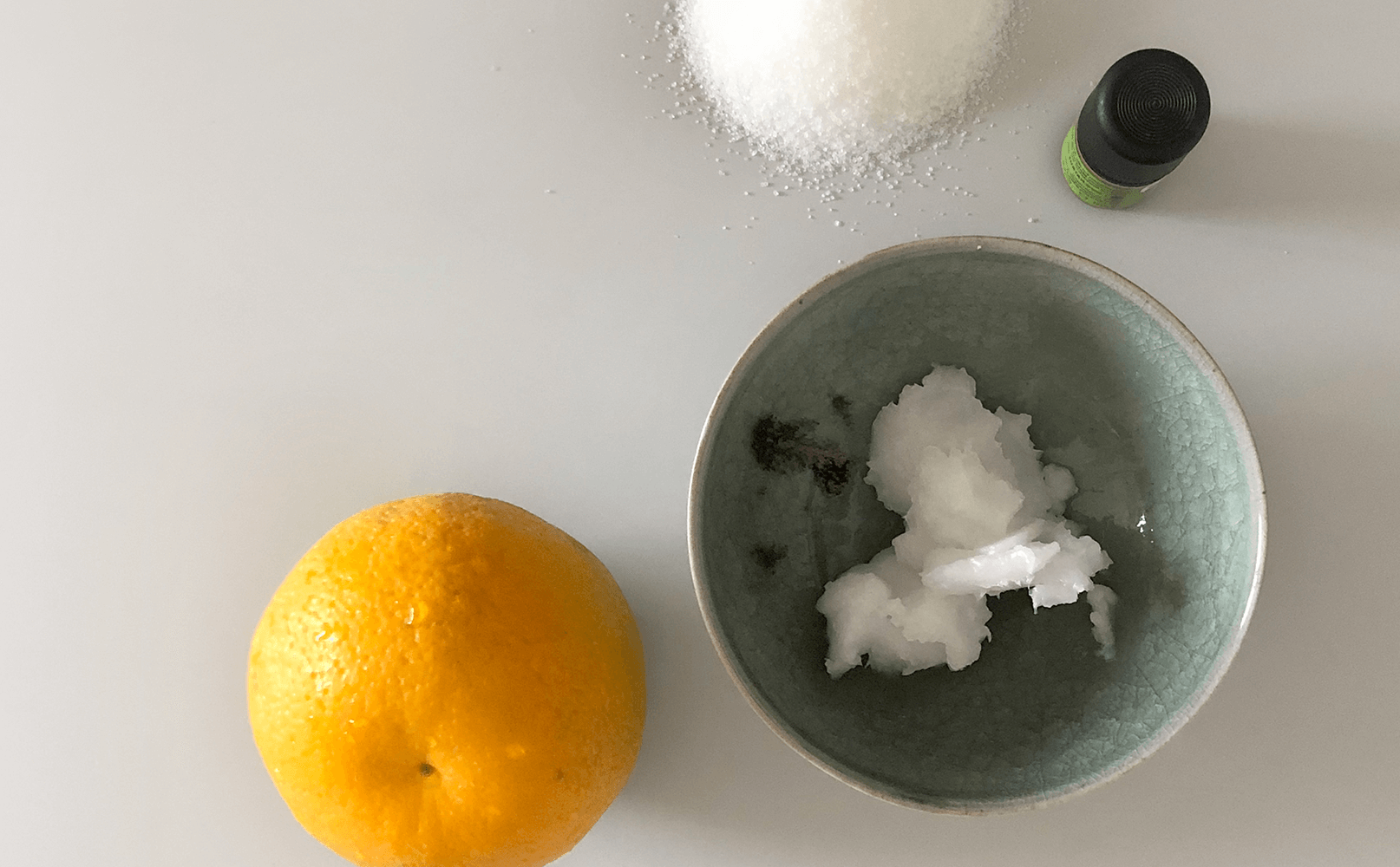 Zutaten für ein DIY-Kosmetikprodukt: Eine Orange, ein Schälchen mit Kokosöl, Zucker, eine kleine Flasche ätherisches Öl.